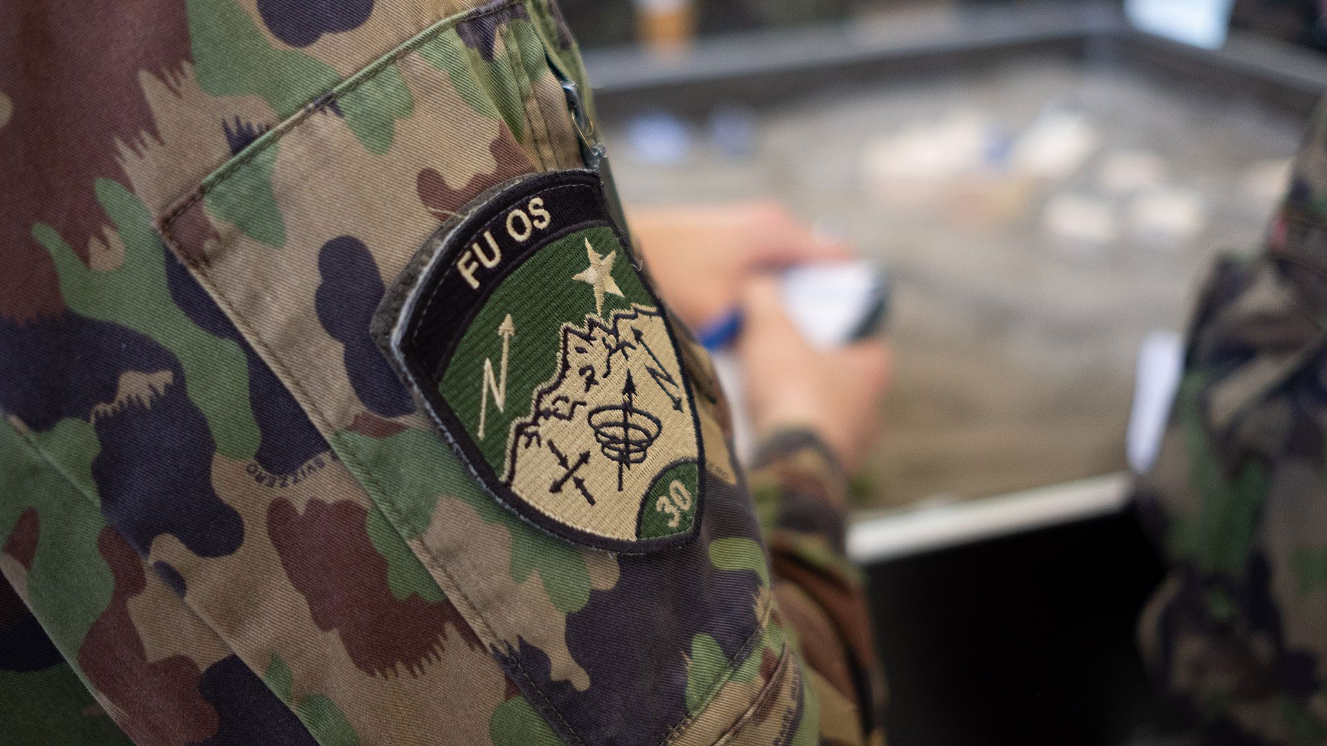 Badge eines Aspiranten der Führungsunterstützungs-Offiziersschule 30, im Hintergrund der Taktik-Sandkasten.